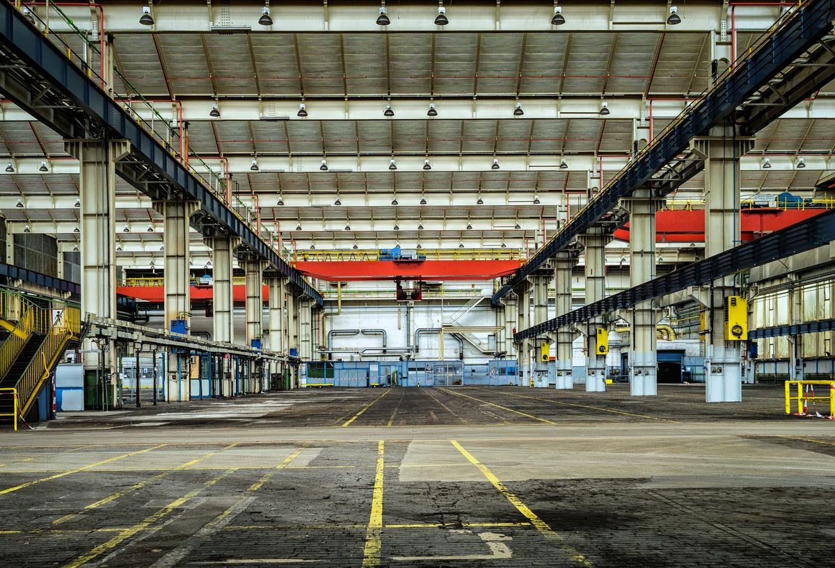 Large empty factory hall with steel columns, overhead cranes and yellow floor markings